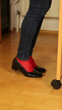 Pés de nylon vermelhos em saltos brilhantes pretos - pendurados e provocando em jeans apertados