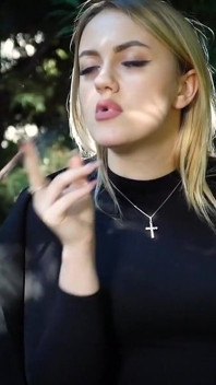 Quente loira gata fumando dois cigarros pretos na natureza