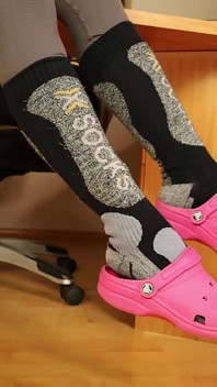 Leggings grises, zuecos rosados, calcetines y descalzo debajo del escritorio