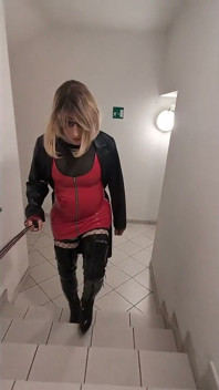 Promenade dans une maison de parking, une blonde dans des bottes overknee, robe en pvc rouge et long manteau de cuir