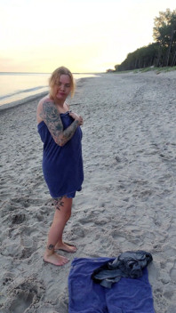 En primer plano. Usted mira como una modelo tetona, de su presencia, se desnuda en la playa, se baña, y juega en la arena.