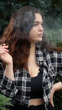 Une douce bombasse russe à forte poitrine fume une cigarette dans la nature