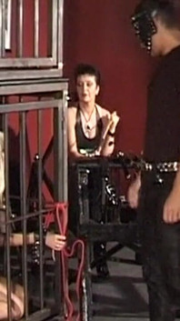 Mature Dominatrix Oversees Masked Man with Bound Blonde