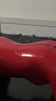Ședință foto în costum de latex roșu cu mască de latex și față transparentă.