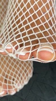 Chica de ébano muestra sus pies con pedicura francesa en sus medias de red blancas