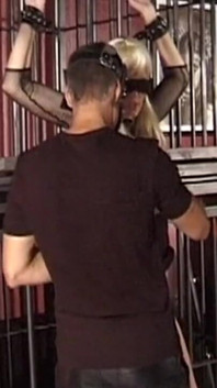 Une dominatrice mature surveille un homme masqué avec une blonde attachée