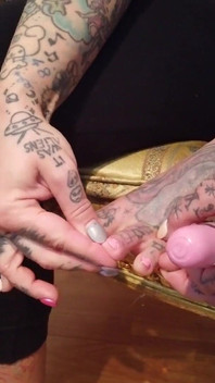 Tetovaná blonďatá dáma si maluje nehty