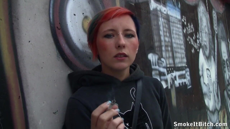 Smoke it bitch: Девушка с цветными волосами и с пирсингом на лице курит сигару на тротуаре улицы
