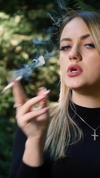 Sexy blondýna Kotě kouří jednu černou cigaretu v přírodě