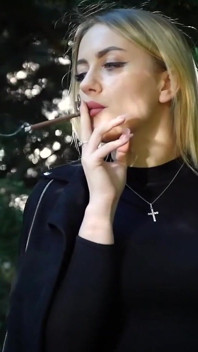 Une bombasse blonde sexy fume deux cigarettes noires dans la nature