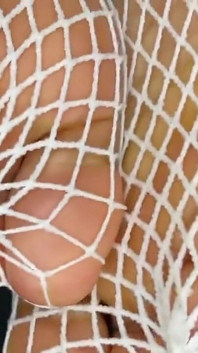 Chica de ébano muestra sus pies con pedicura francesa en sus medias de red blancas