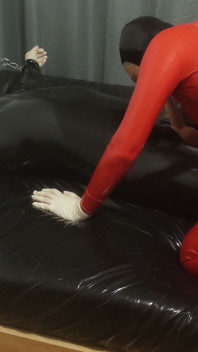 Une MILF Sexy Dans Une Combinaison En Latex Rouge Elle S’amuse Avec Un Esclave Enfermé. Deuxième Angle