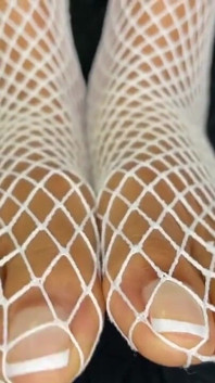 La ragazza ebano mostra i suoi piedi con una pedicure francese nelle sue calze a rete bianche