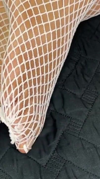 La ragazza ebano mostra i suoi piedi con una pedicure francese nelle sue calze a rete bianche