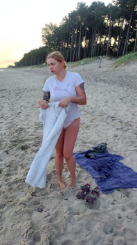 En primer plano. Usted mira como una modelo tetona, de su presencia, se desnuda en la playa, se baña, y juega en la arena.