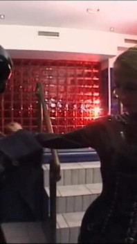Blonde penis met grote borsten vernederd, voet uitrekkend in latex jurk in gemaskerd