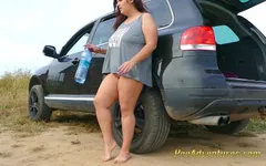 Une grosse brune aux seins énormes fait pipi par terre s'appuyant sur la voiture