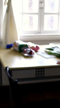 Asiática gata em um espartilho vermelho brinca com um pepino na mesa da cozinha