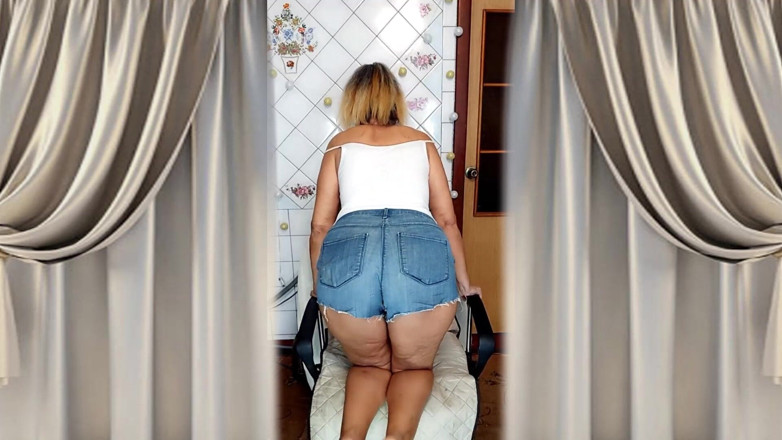Lukerya: Starší babička se šedými vlasy škádlí svou postavou a nohama v kuchyni.