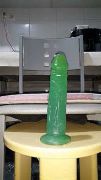 Knullar min rumpa med en enorm grön dildo i bakgrunden Närbild